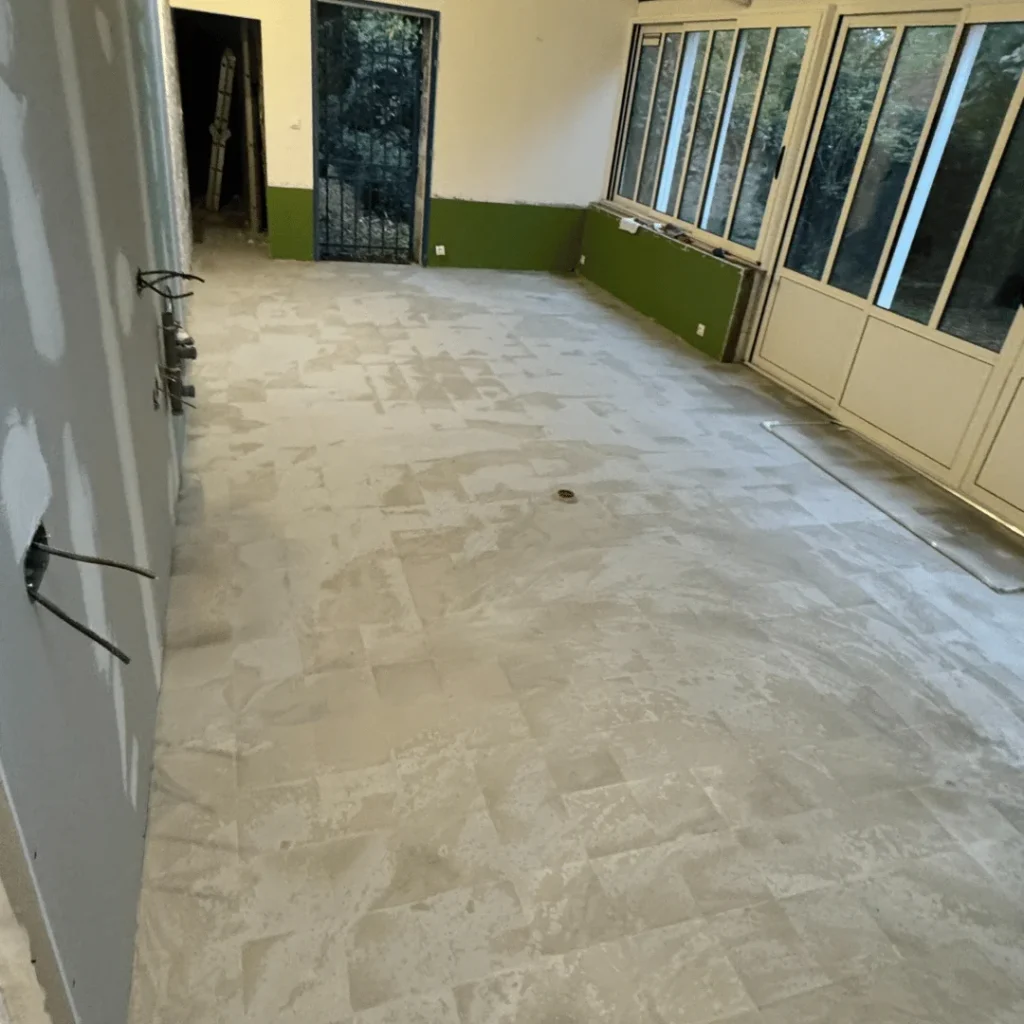 Pose de carrelage grand format en cours dans une véranda