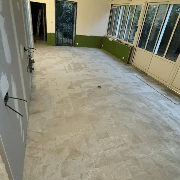 Pose de carrelage grand format en cours dans une véranda